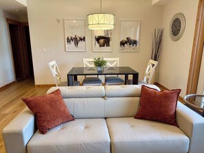 Ein Wohnzimmer mit einer Couch, zwei roten Kissen, einem Esstisch mit Stühlen und Wandbildern.