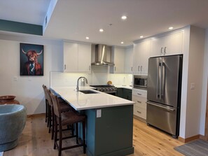 A modern kitchen with a central island, stainless steel appliances, and a herringbone-patterned backsplash. - Mountain Lynx Retreat | Spring Creek King Suite (Canmore)