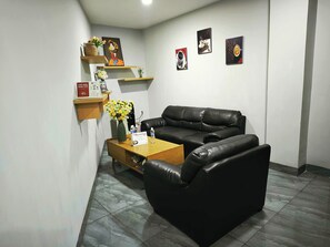Una sala moderna con un sofá de cuero negro, una mesa de centro de madera y estanterías con adornos.