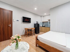 A compact hotel room with a bed, a small dining table with chairs, a kitchenette, and a TV mounted on the wall. - YOUR HOME - Quiet Studio 30m² (Ho Chi Minh City)