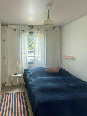 A bedroom with a bed, a bedside table, a lamp, a ceiling fan, and a window with curtains. - Summer cottage with orangery and garden, Falster (Væggerløse)
