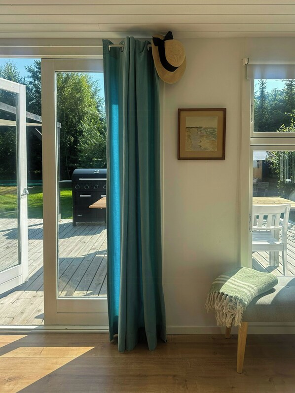 Une pièce dotée d’une porte-fenêtre coulissante, d’une terrasse en bois, d’un tableau encadré accroché au mur et d’un chapeau suspendu à la porte.
