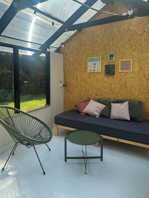 Ett rum med ett glastak, en vägg av trä, en soffa med kuddar, en grön stol och ett litet bord.