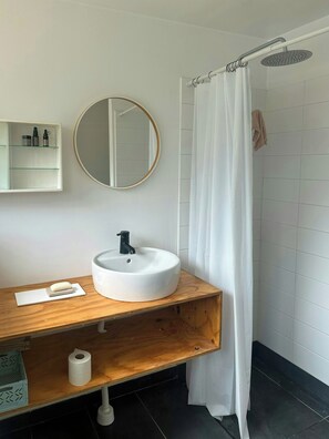 Een badkamer met een ronde spiegel, een witte wastafel, een houten meubel en een douchegordijn.