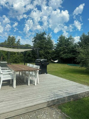 En träaltan med ett bord och stolar, en grill och en hängmatta.
