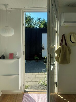 Une porte ouverte donnant sur une cour intérieure où se trouvent un pot de fleurs, un chapeau suspendu et un sac.