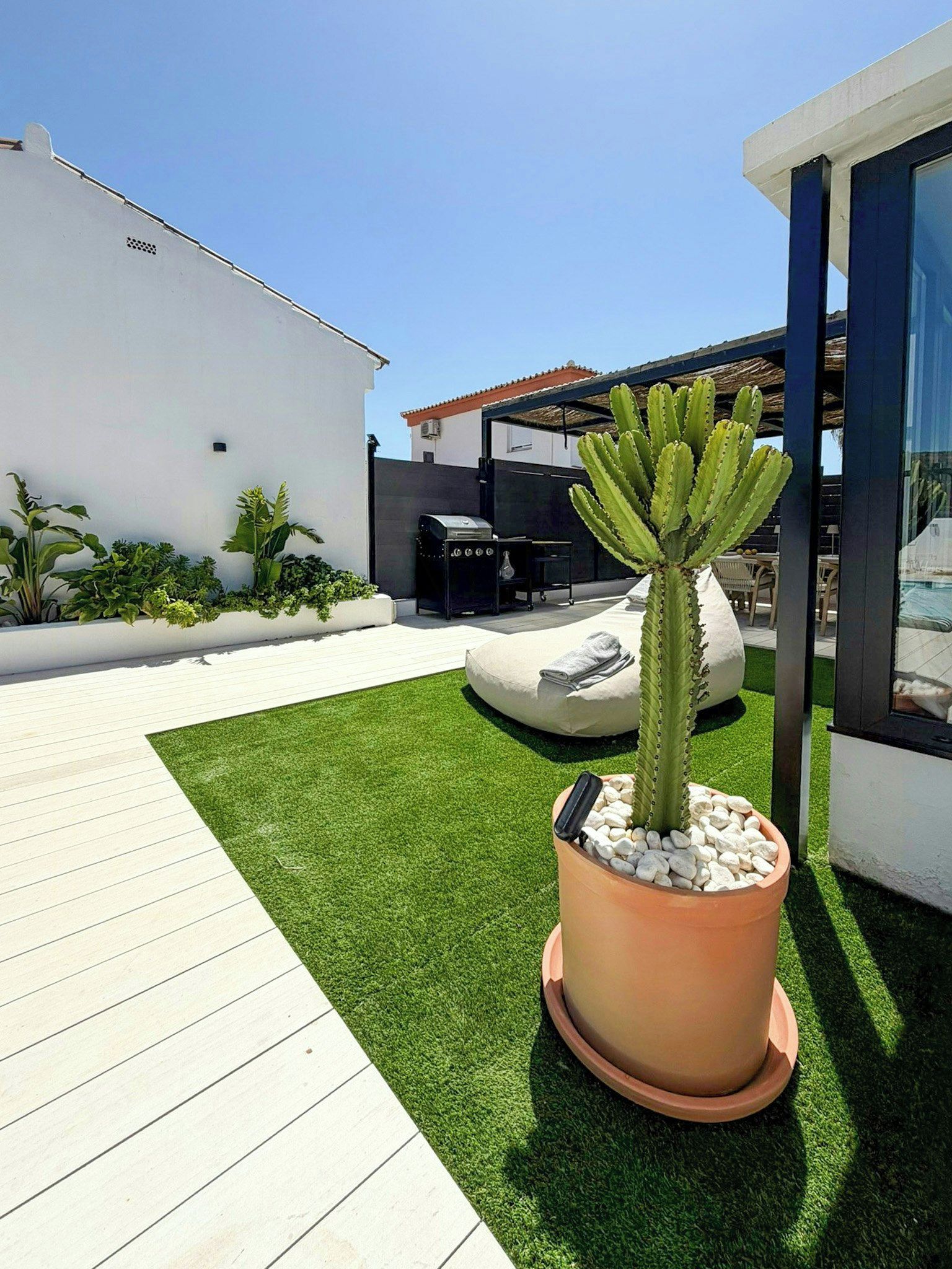 Eine moderne Außenpatio mit künstlichem Gras, einer großen Kübelkaktus und einem Grill.
