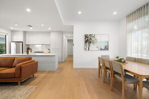 Une cuisine moderne avec des meubles blancs, un îlot central et un coin repas comprenant une table et des chaises en bois.