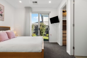 A bedroom with a bed, a TV mounted on the wall, a sliding glass door leading to a garden, and a closet with a mirror. - Somerton Days Contemporary Escape near the Beach (Somerton Park)