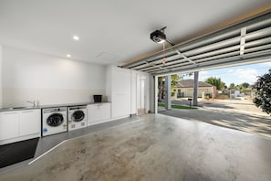 Une buanderie moderne équipée d’un lave-linge, d’un sèche-linge et d’une grande fenêtre donnant sur la rue.