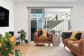 A modern living room with a brown leather sofa, a coffee table, and a TV mounted on the wall. - Somerton Days Contemporary Escape near the Beach (Somerton Park)