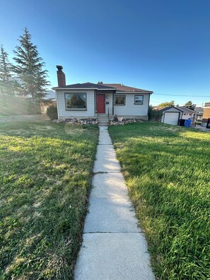 A residential house with a red door, a front yard, and a clear sky. - Millcreek MTN Home. - 2 bdm 1 bth, full kitchen, (Salt Lake City)