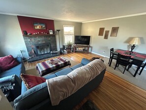 Ein Wohnzimmer mit Kamin, einer Couch, einem Fernseher und einem Essbereich.