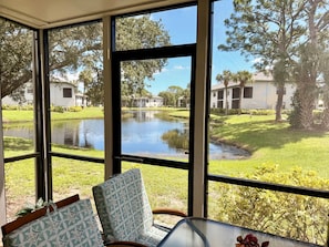 Ein Zimmer mit großem Fenster mit Blick auf einen Teich und Gebäude. Ein Tisch mit einem Stuhl und einer Tasche sind ebenfalls vorhanden.