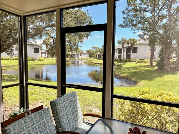 A room with a large window overlooking a pond and buildings. There is a table with a chair and a bag. - MB-near Beaches and IMG, Pool, Tennis, Pickleball (Bradenton)