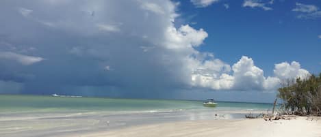 A beach with clear turquoise water, a sandy shore, and a partly cloudy sky.