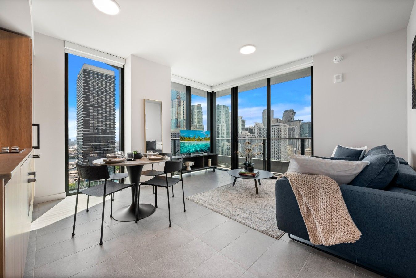 A modern living room with a dining area, large windows with city views, and a cozy seating area.