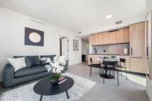 Ein modernes Wohnzimmer mit einem grauen Sofa, einem Couchtisch mit Pflanze und einem Essbereich mit kleinem Tisch und Stühlen.