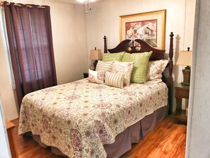 Un dormitorio con colcha estampada, cabecera de madera, dos lámparas de noche y un cuadro en la pared.