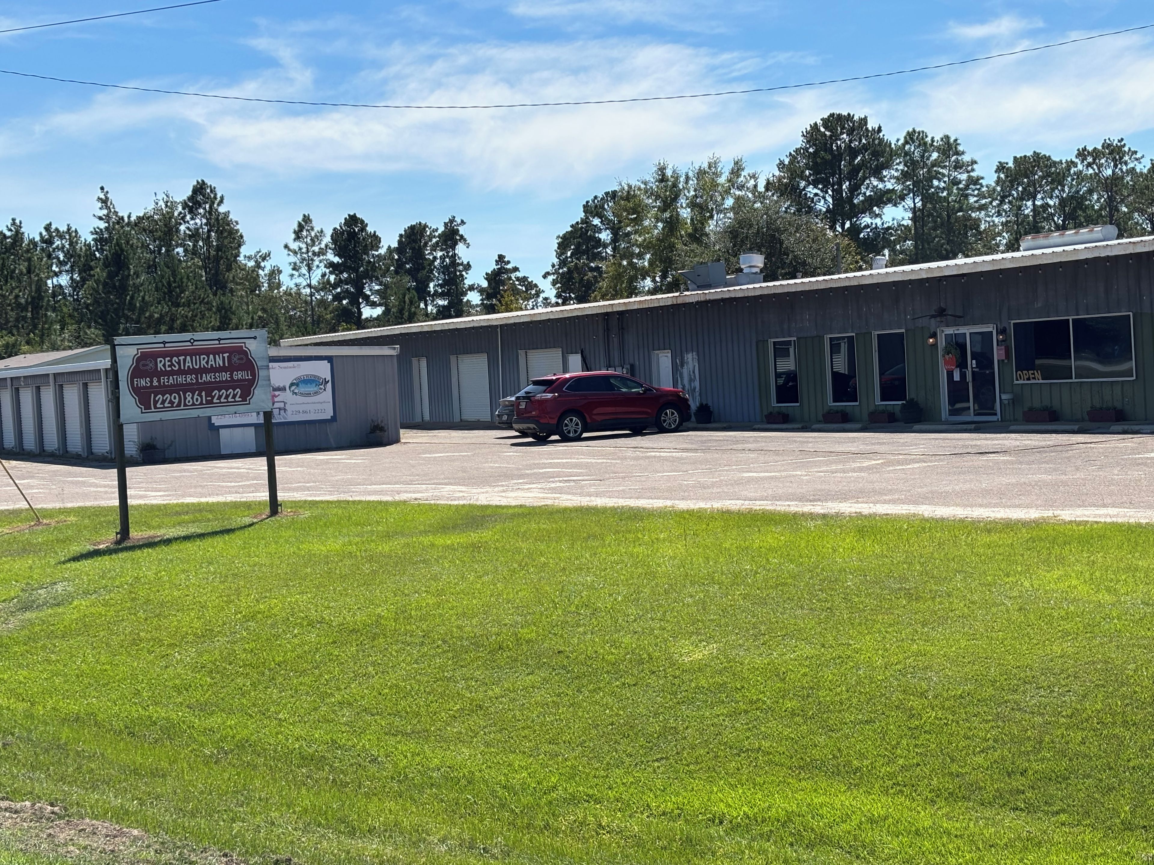 A restaurant with a signboard, a red car parked in front, and a building with a flat roof.