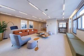 Un moderno vestíbulo de hotel con un sofá modular, un sillón gris, una mesa de centro y una zona de bar.