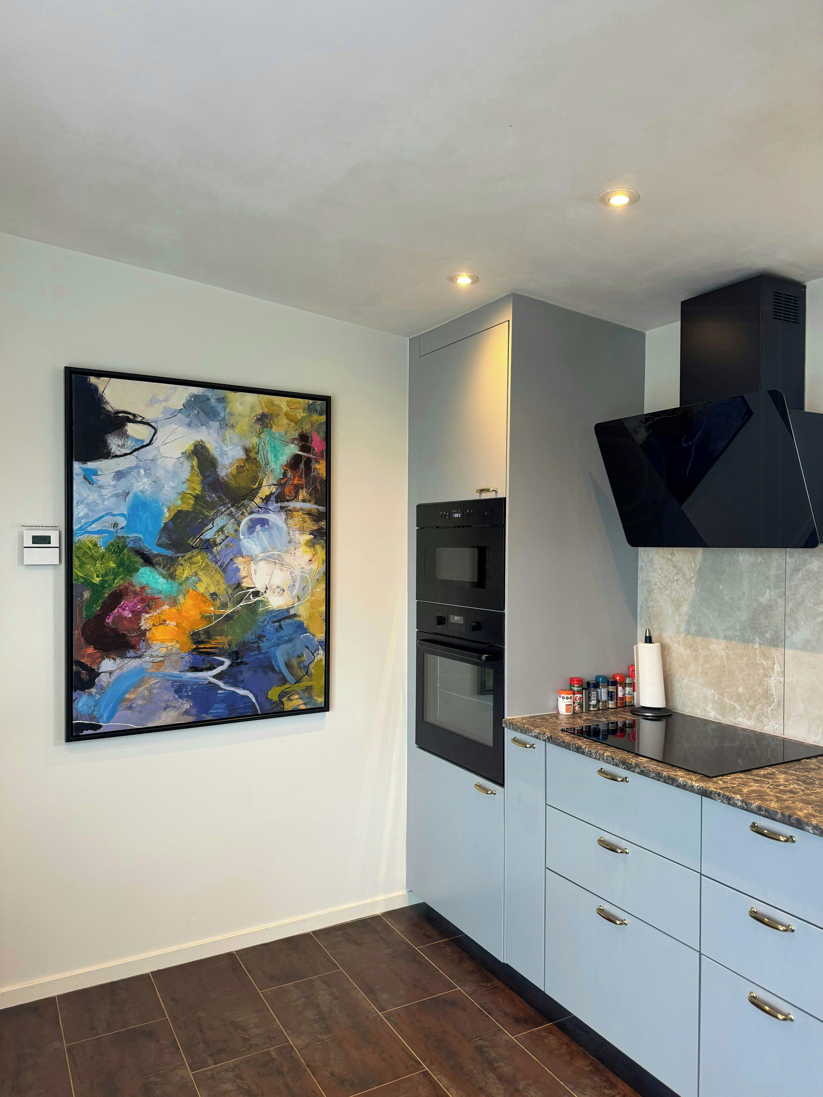 Una cocina moderna con un cuadro abstracto grande, electrodomésticos integrados y encimera de mármol.