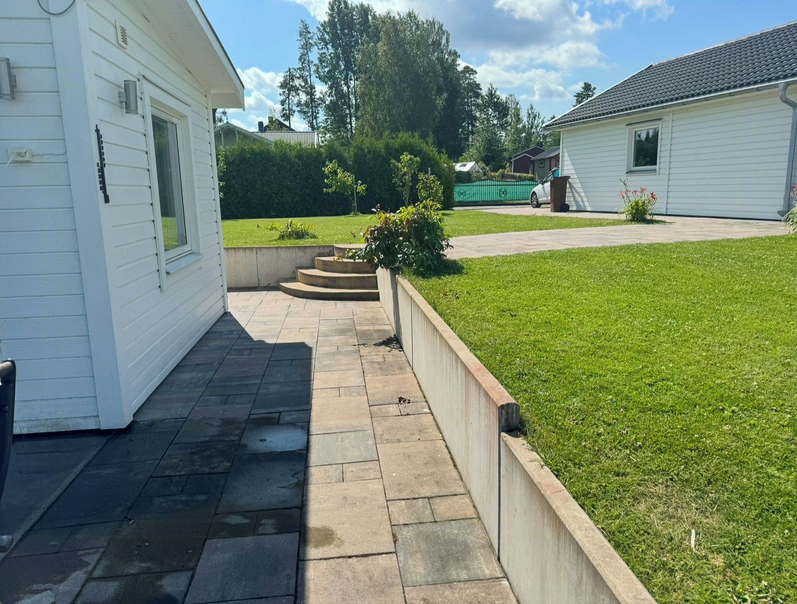 A residential property with a paved patio, a grassy lawn, and a small garden area with steps leading to a door.