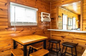 A wooden interior with a table and stools, a window with blinds, and a wall-mounted sign reading 'VINO'. - Lake Geneva Getaway Home | Walk to Downtown & Lake (Lake Geneva)