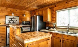 A wooden cabin interior with a kitchen area, including a refrigerator, oven, and wooden cabinets. - Lake Geneva Getaway Home | Walk to Downtown & Lake (Lake Geneva)