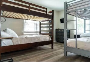 A bunk bed room with a wooden bunk bed and a metal bunk bed, a dresser, and a television on the wall. - Lake Geneva Getaway Home | Walk to Downtown & Lake (Lake Geneva)