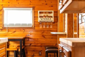 Un interior de madera con una mesa, sillas, una ventana y un letrero que dice 'VINO'.