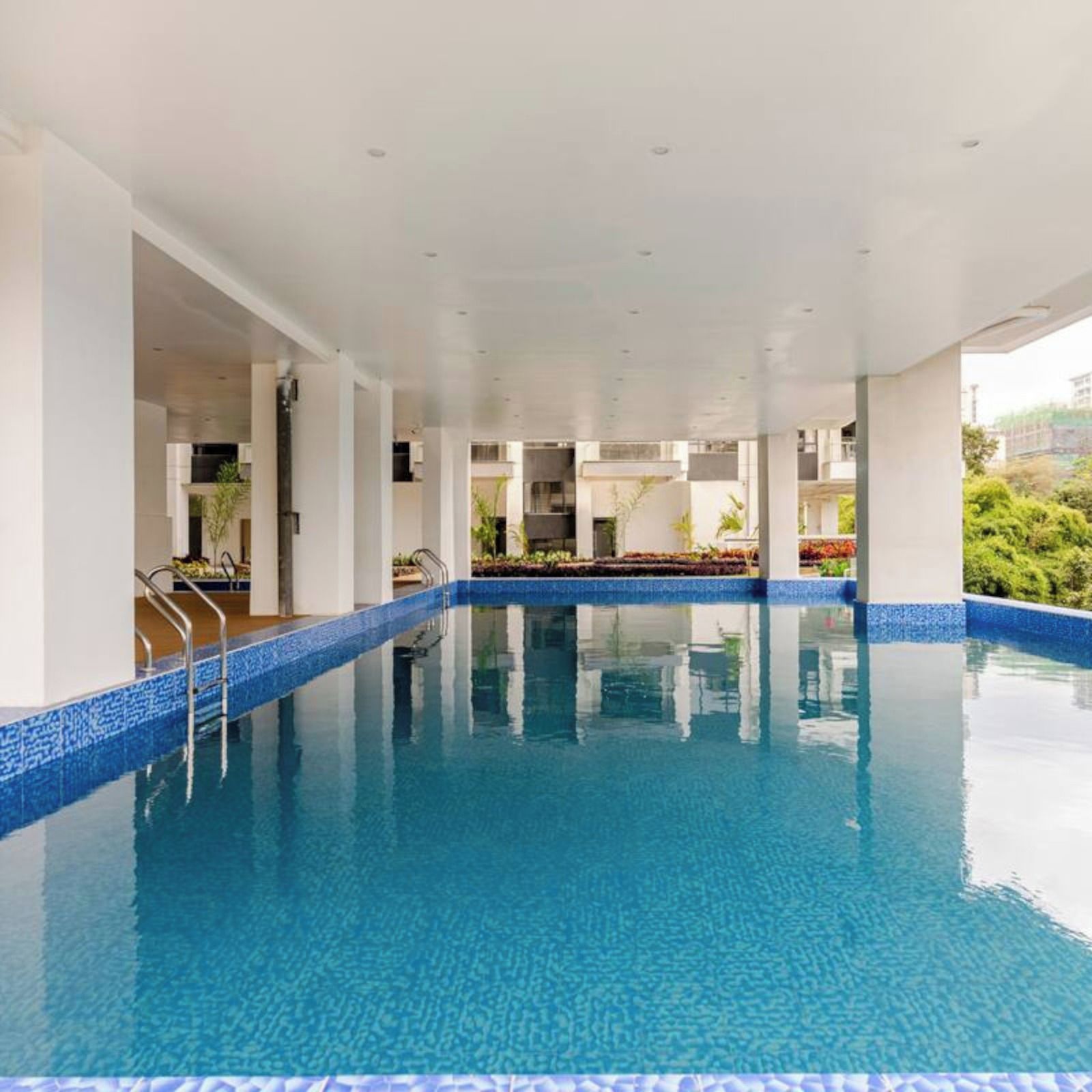 A large indoor swimming pool with clear blue water, surrounded by white pillars and a tiled edge.