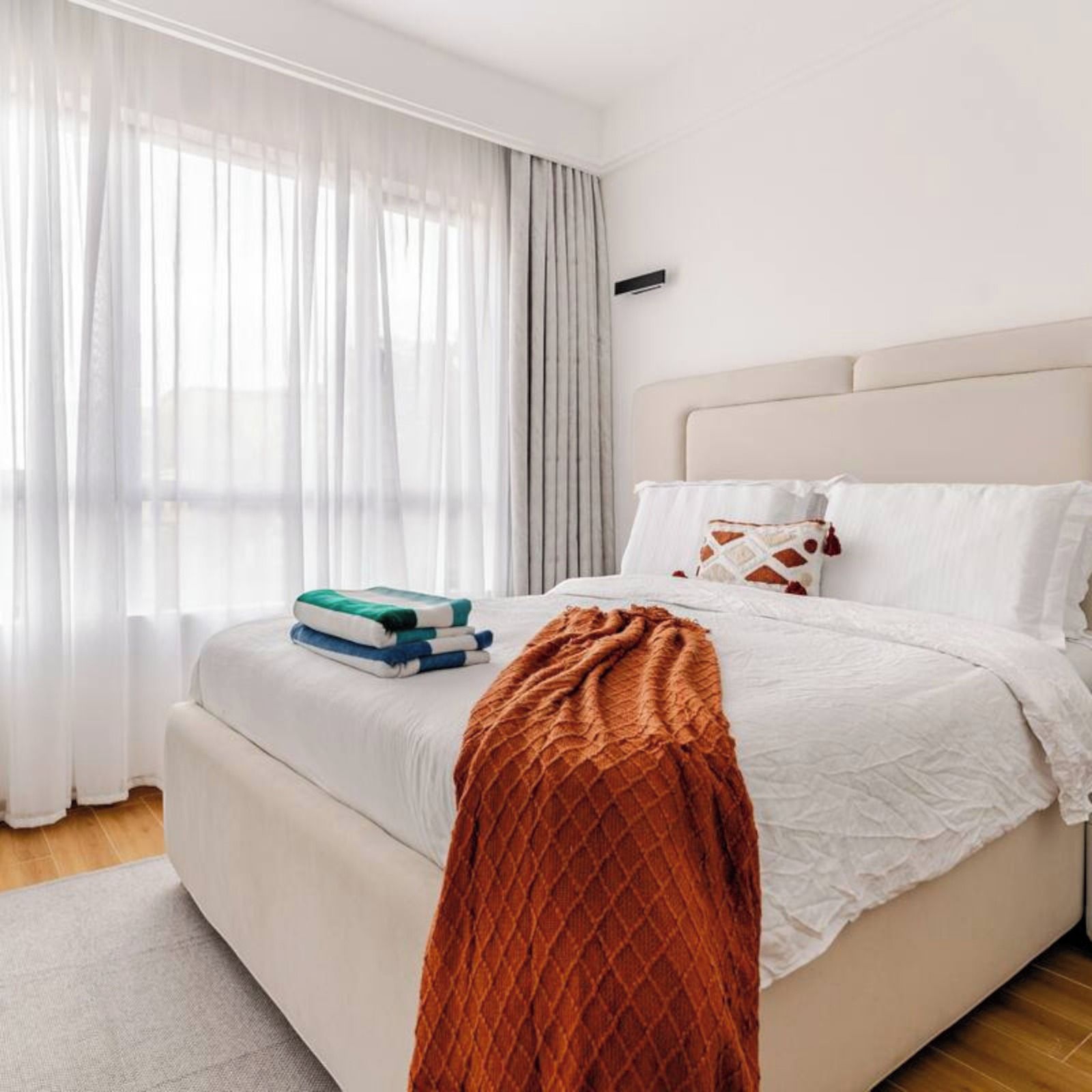 A bedroom with a bed, white bedding, a brown throw blanket, and a stack of books.