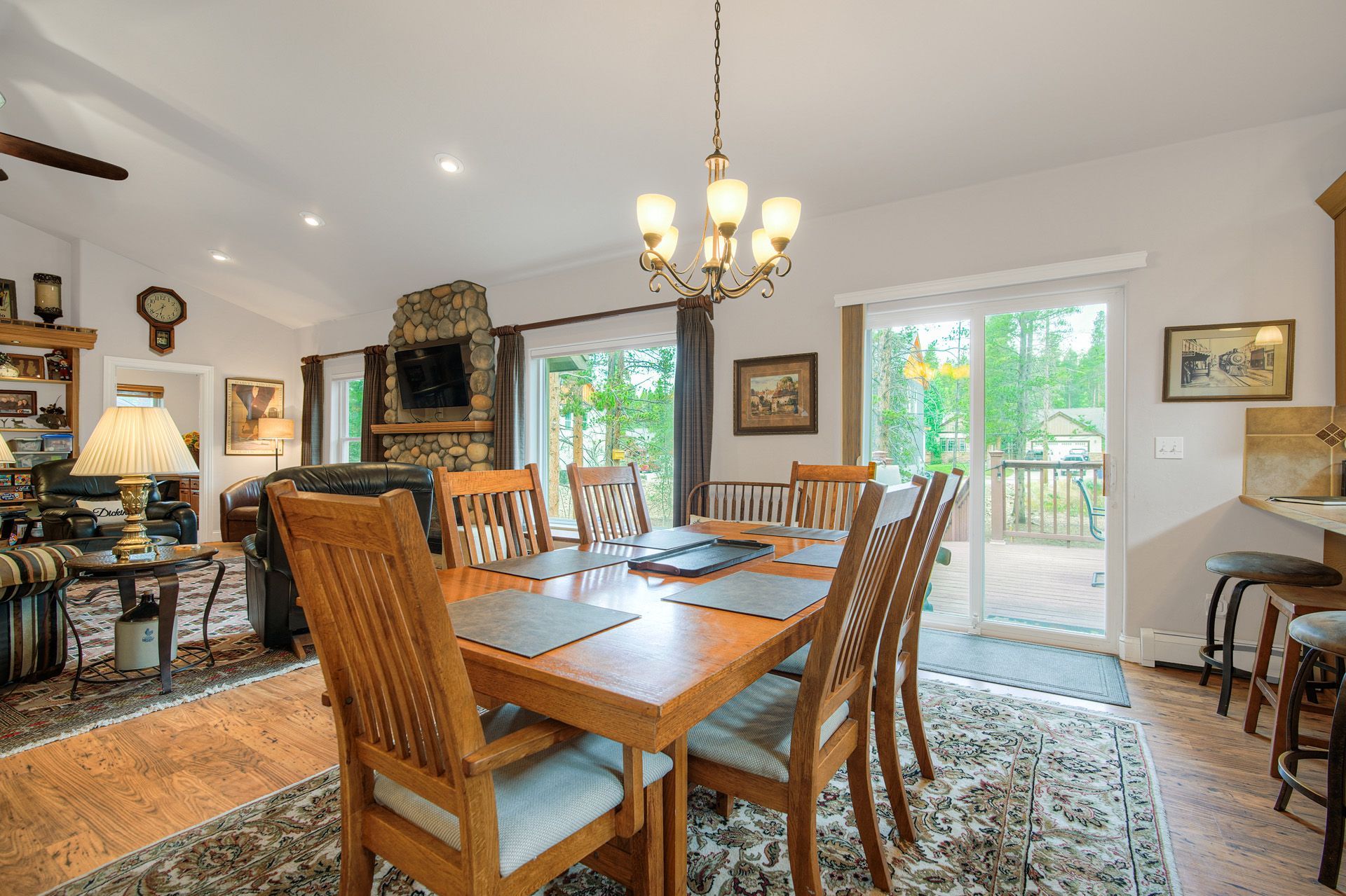 A dining area with a wooden table and chairs, a stone fireplace, a television, and a view of the outdoors.