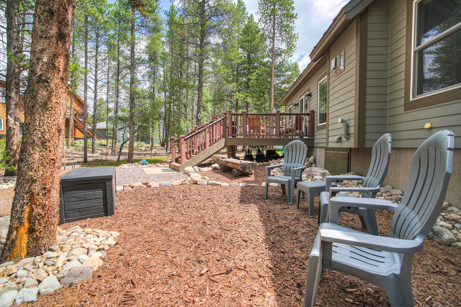 Une terrasse en bois avec des chaises, un chemin de pierre et une maison dotée d’une terrasse.