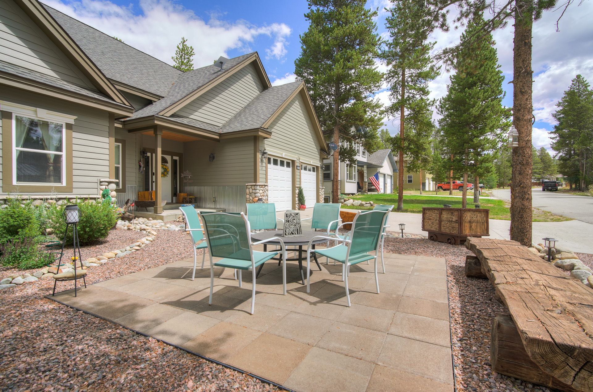 A residential house with a covered patio area featuring a table and chairs, surrounded by a garden with a stone border.