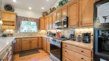 A modern kitchen with wooden cabinets, stainless steel appliances, and a large window with a view of greenery.