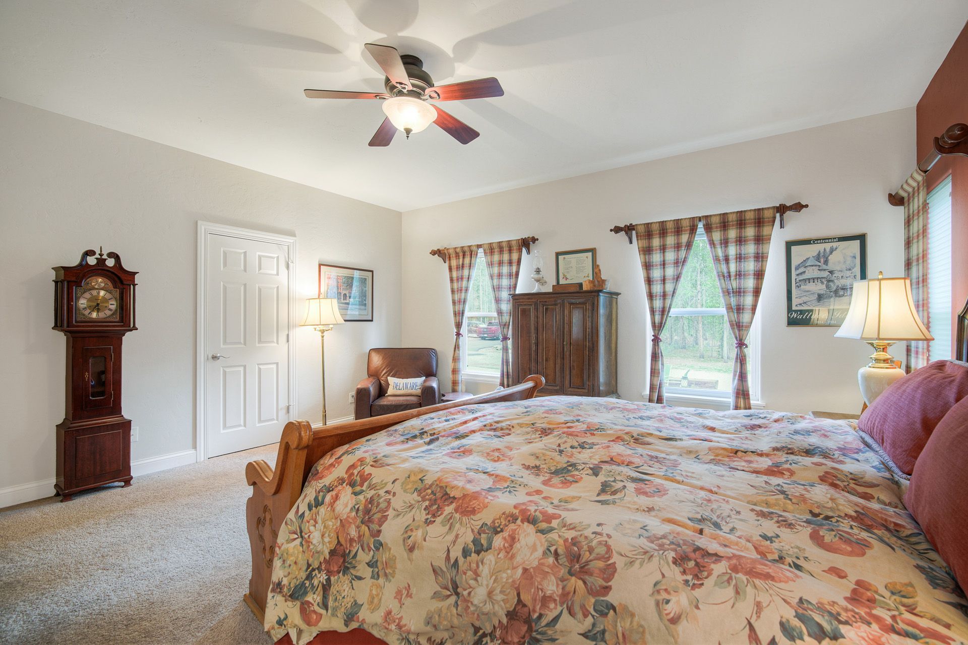 A bedroom with a bed, a ceiling fan, a clock, and a window with curtains.