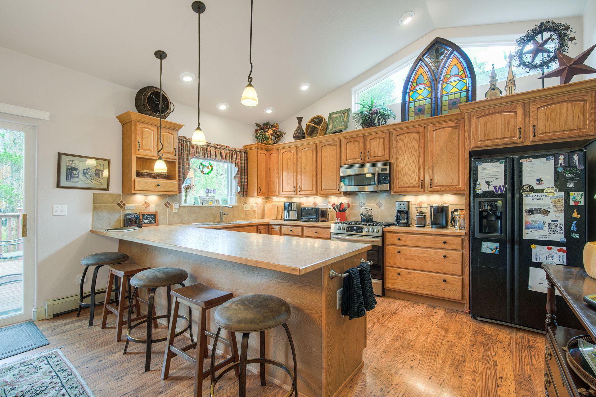 A spacious kitchen with wooden cabinets, a large island with stools, a built-in oven, and a refrigerator with magnets.