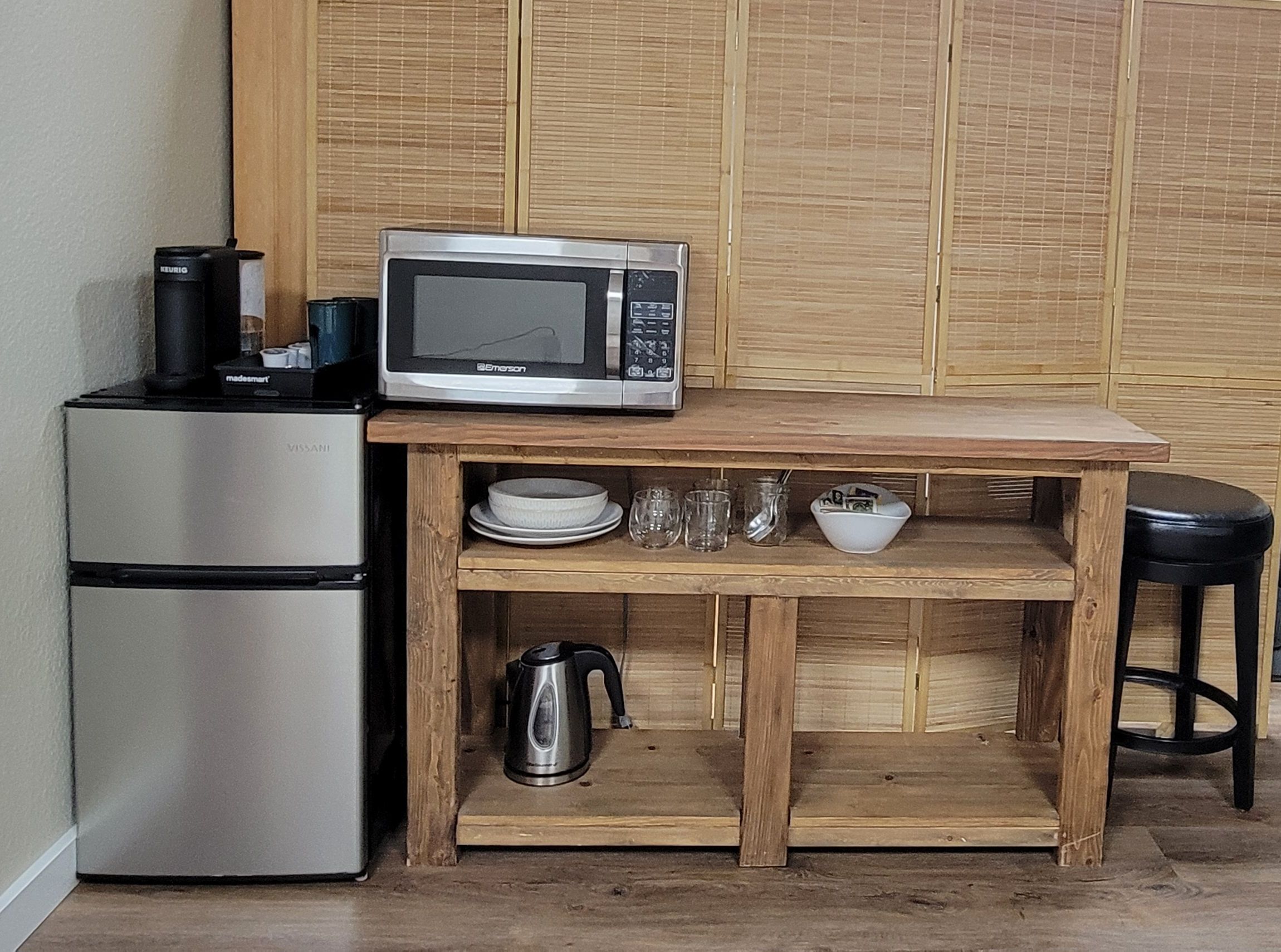 A compact kitchenette with a microwave, a coffee maker, and a kettle on a wooden countertop.