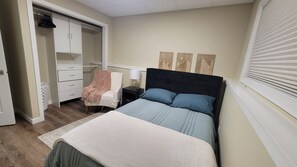 Quarto com cama, cadeira, mesa de cabeceira, guarda-roupa e janela com persianas.
