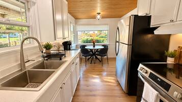 Una cocina moderna con un lavamanos de acero inoxidable, un refrigerador negro y una zona de comedor con mesa y sillas.