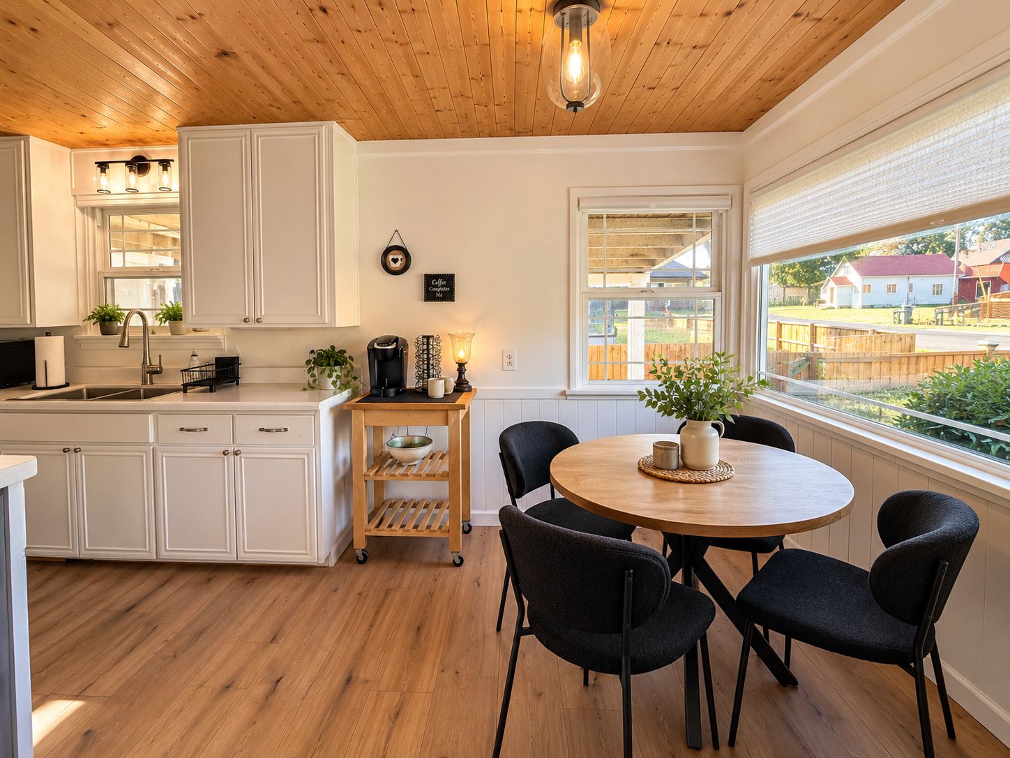 Una cocina con armarios blancos, encimera de madera, estación de café y comedor con mesa redonda y sillas.