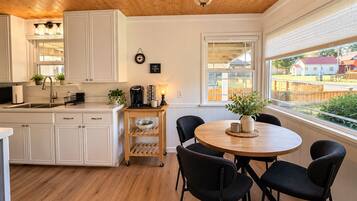 Una cocina con armarios blancos, encimera de madera, estación de café y comedor con mesa redonda y sillas.