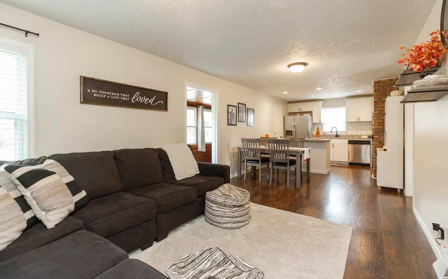 A modern living room with a dark brown sofa, a white rug, and a dining area with wooden chairs and a table.
