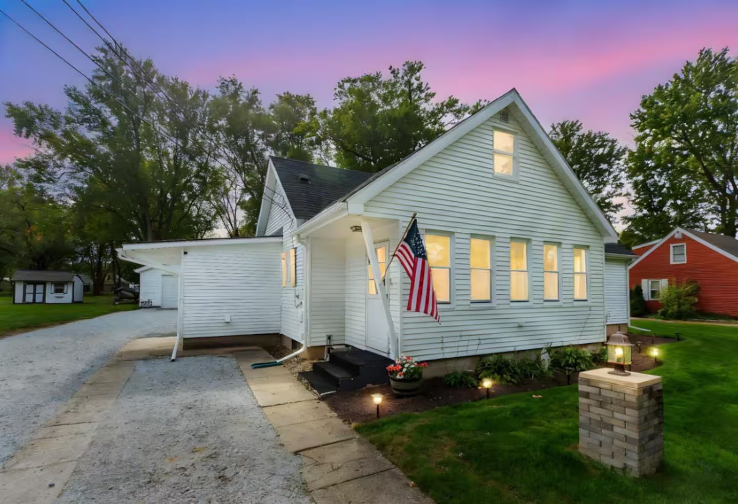 A single-story house with a front porch, a flag, and a well-lit entrance.