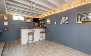 Zona de bar con dos taburetes, una barra y una pared decorada con cuadros y carteles.