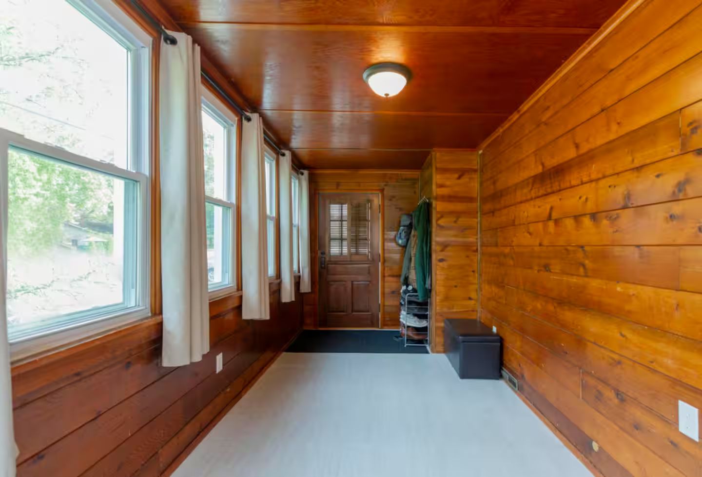 A wooden hallway with a door at the end, large windows on one side, and a ceiling light.