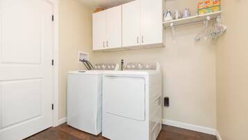 A laundry room with two white front-loading washing machines, a white door, and a shelf with cleaning supplies.