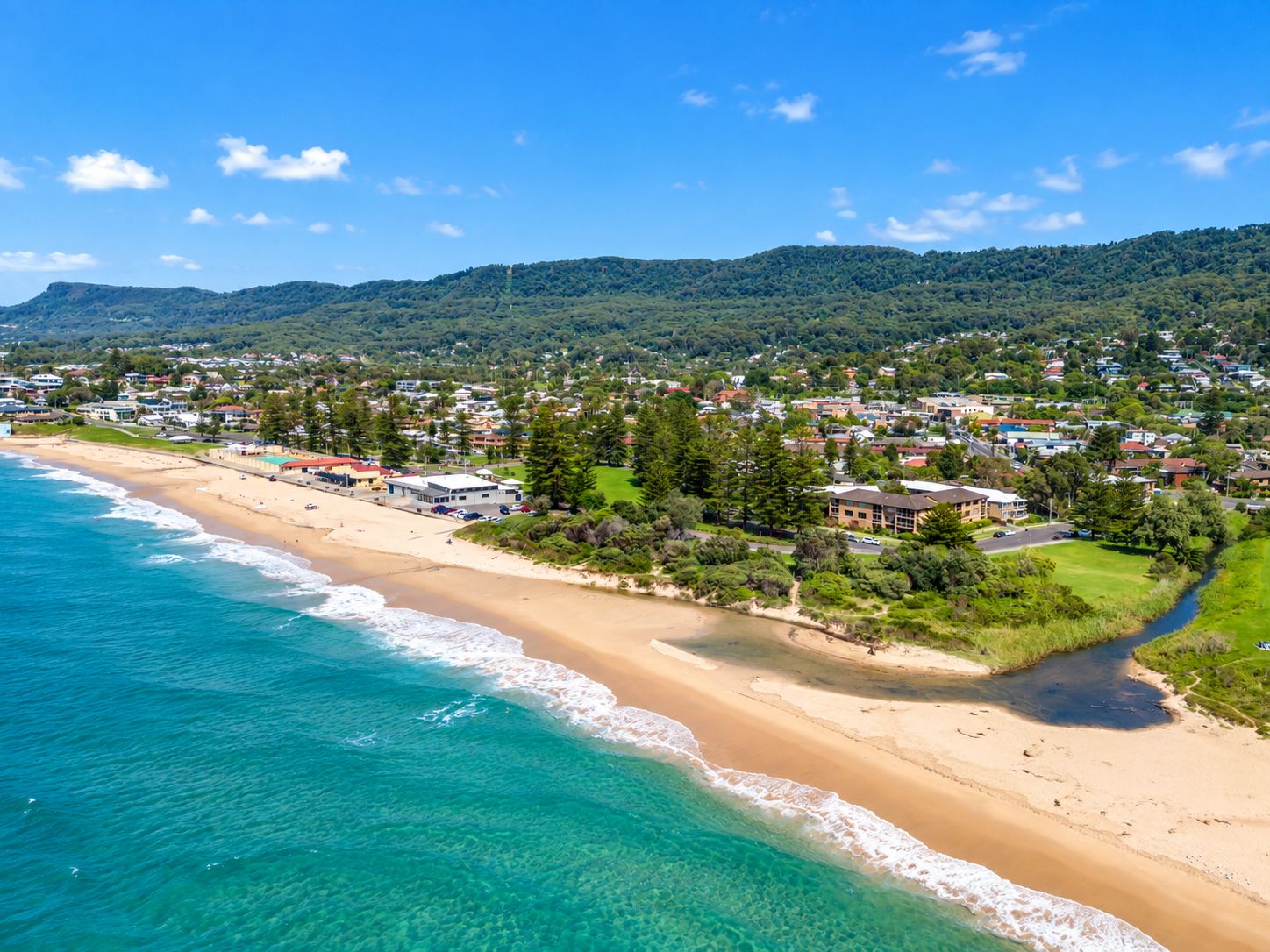 A coastal town with a beach, houses, and a hilly landscape in the background.